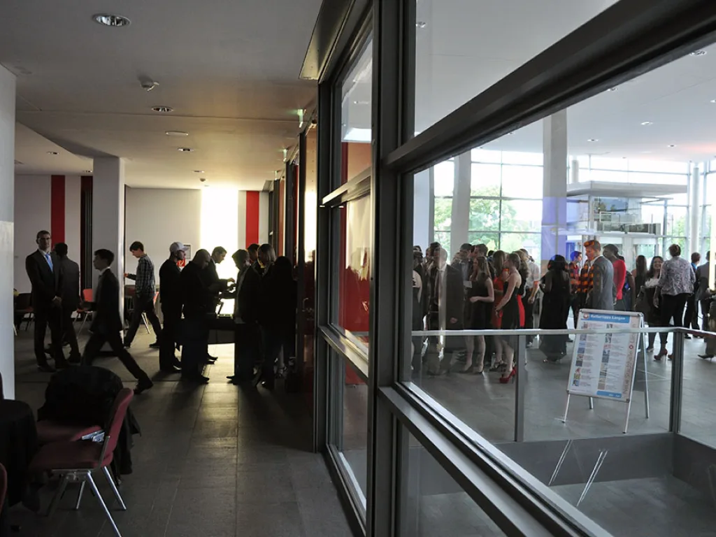 Gäste stehen im Foyer hinter der Glasfassade.